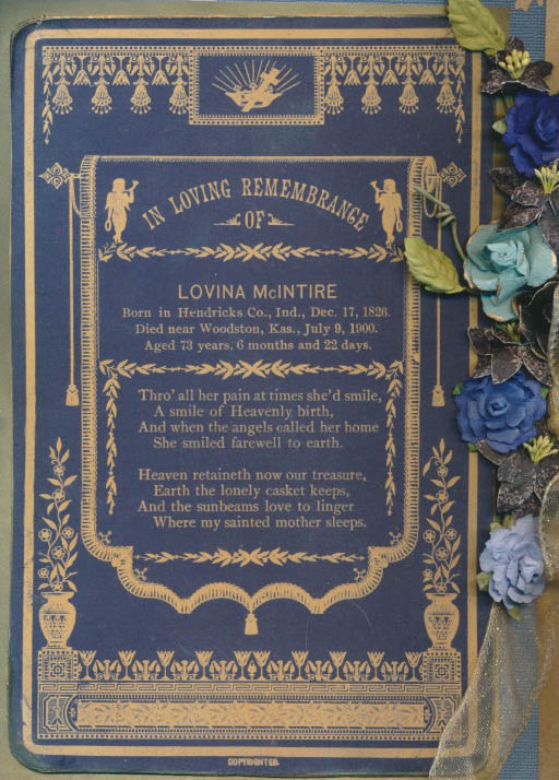 Blue memorial plaque with ornate gold detailing and a floral border, honoring Lovina McIntire; includes a poem and birth/death dates, set beside blue and teal artificial flowers.