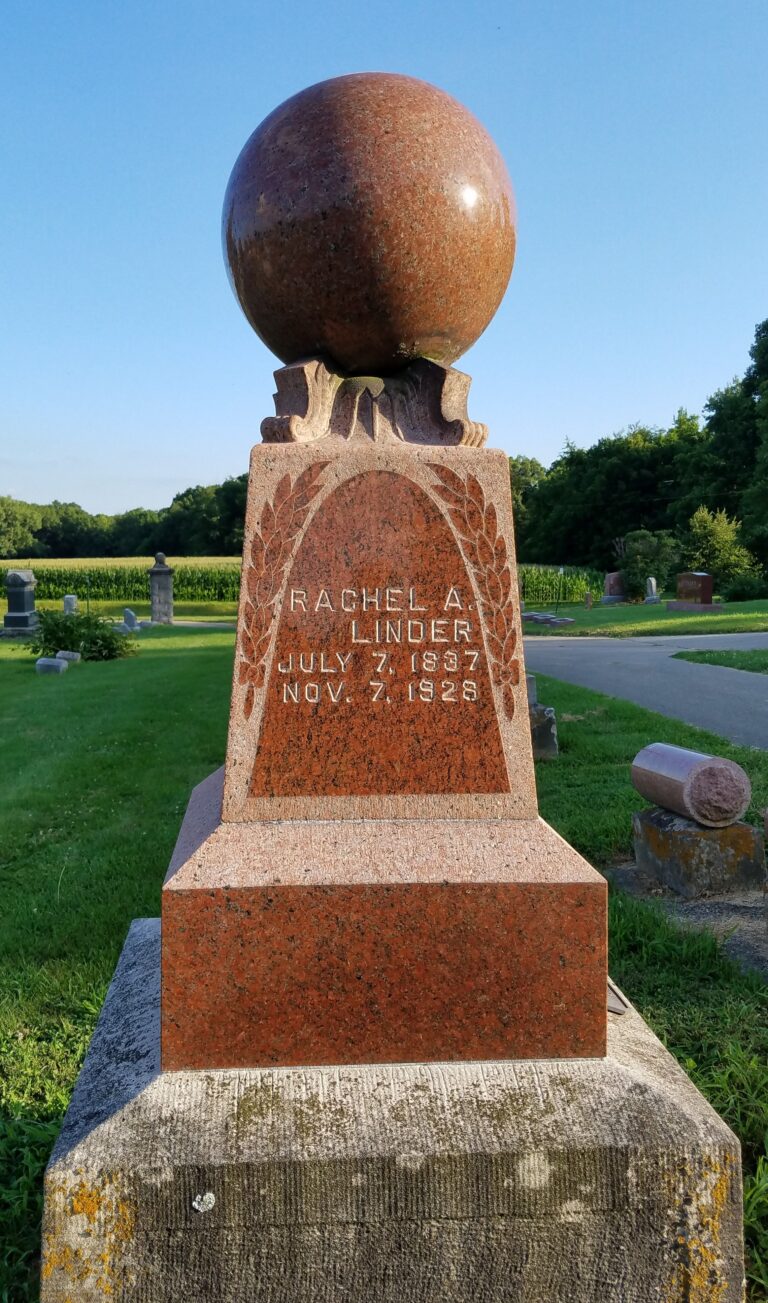 Granite tombstone with a large polished red sphere on top, inscribed Rachel A. Lindner, July 7, 1837 – Nov. 7, 1929, in a cemetery setting.
