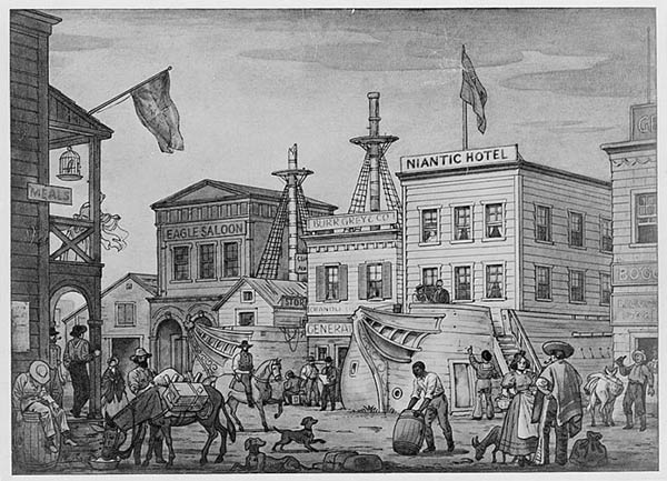 Historic frontier town street with wooden buildings (Niantic Hotel, Eagle Saloon), flags, people, horses, and a docked boat on a riverside set.